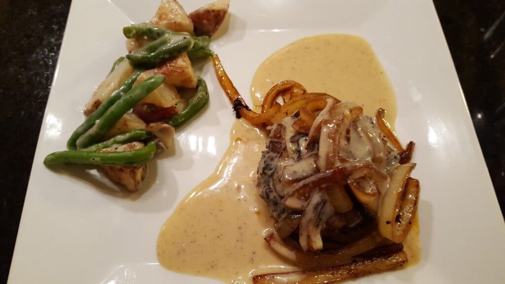 hamburger steak with caramelized onions and green beans on a white plate