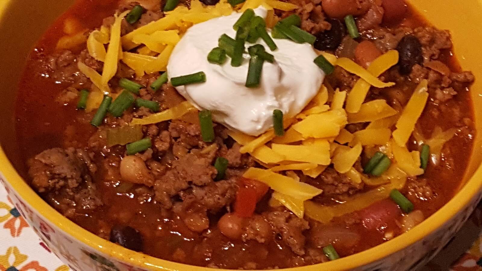 Bowl of Chili with sour cream and shredded cheese with chives on top