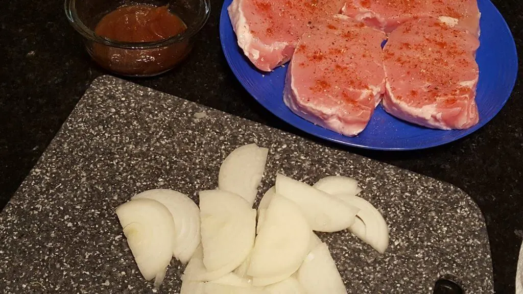 Pork cutlets on a plate with seasoning next to some sliced onions