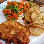 Southern Pan Fried Pork Chops on a plate with fried potatoes, peas and carrots from Julia's Simply Southern