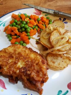 Southern Pan Fried Pork Chops on a plate with fried potatoes, peas and carrots from Julia's Simply Southern