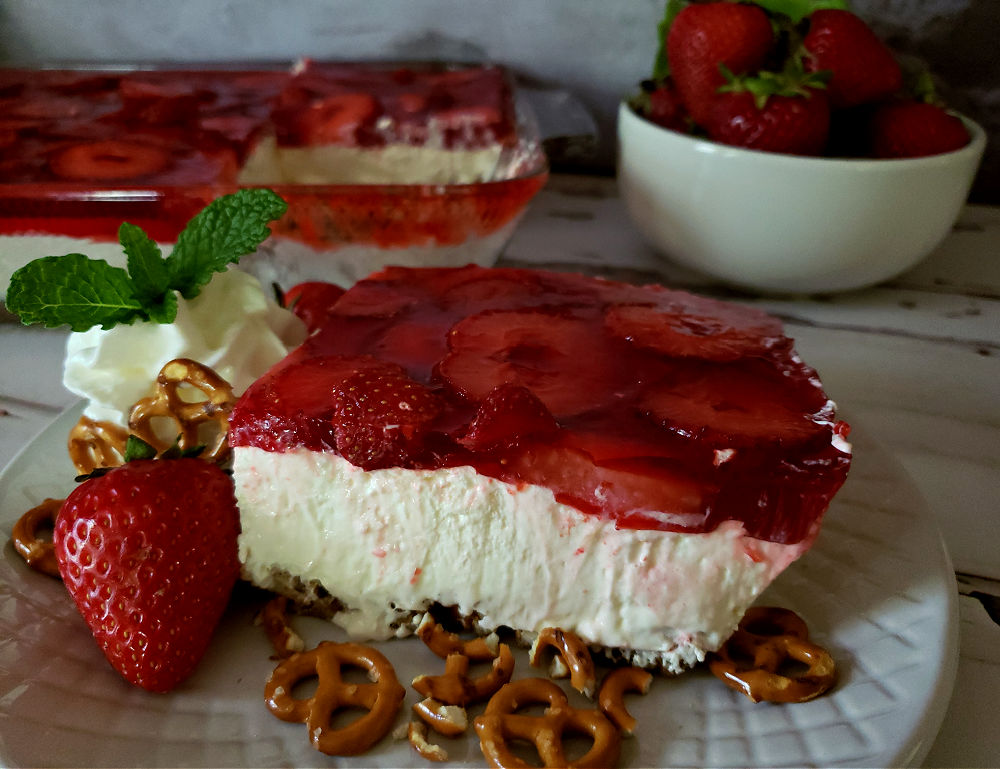 Classic layered dessert of the best strawberry pretzel salad recipe with a bowl of fresh berries in the background