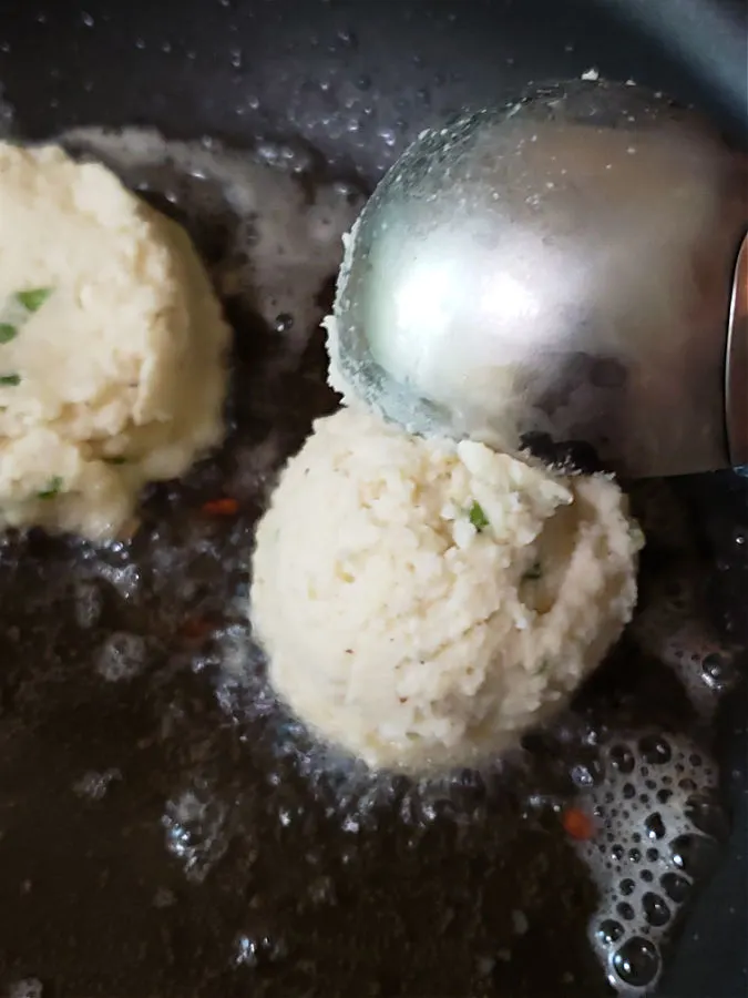 Using a scoop to add the potato cake mixture to a hot cast iron skillet of oil for frying