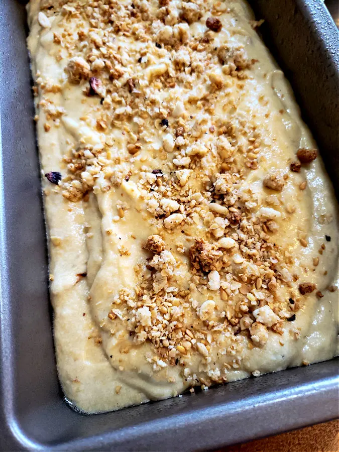 Banana bread batter in a loaf pan topped with granola before baking