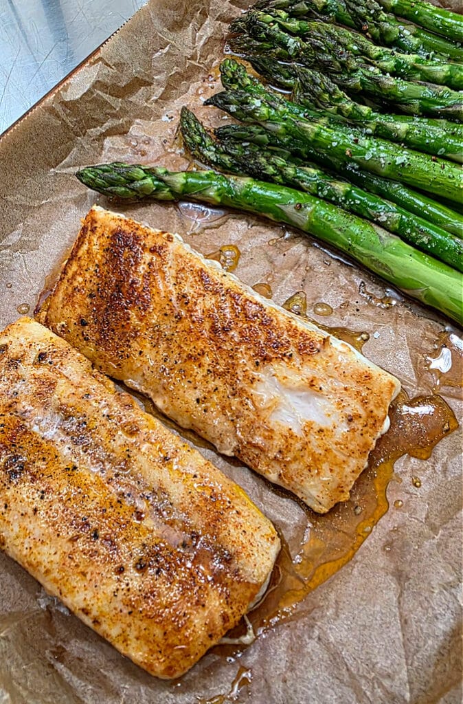 Two pieces of fish on a parchment lined sheet pan with asparagus.