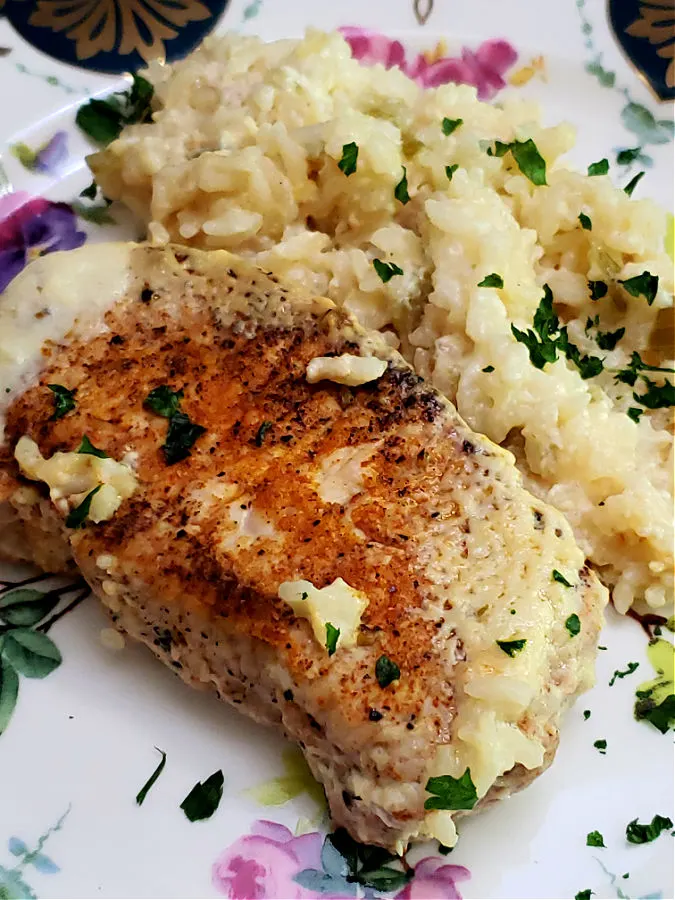 seasoned pork chops with cream of celery baked rice on a floral plate garnished with parsley