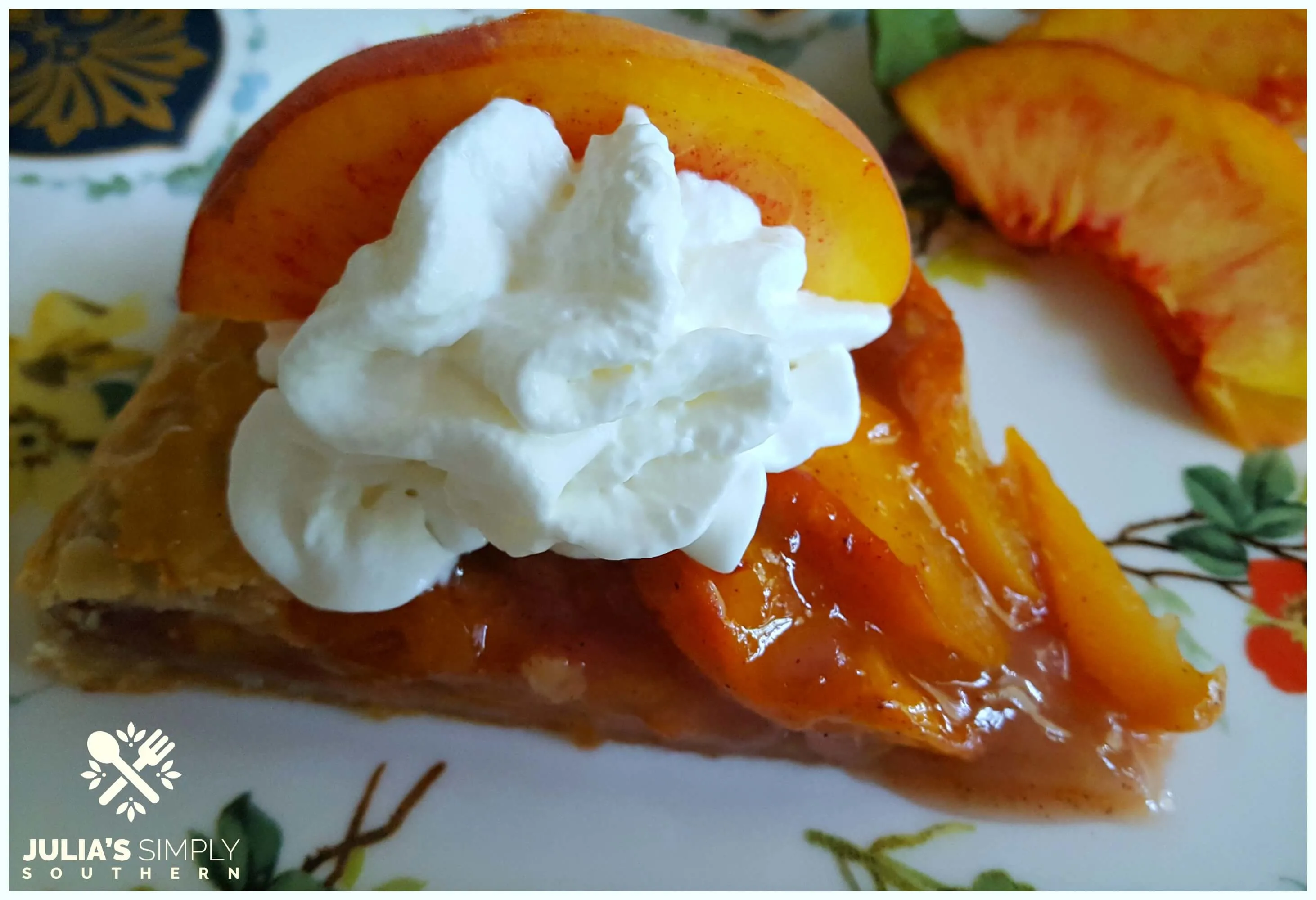 Slice of peach galette with whipped cream and a slice of fresh peach for garnish on a Vanderbilt china plate