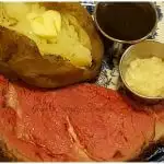 Perfect Prime Rib served on a plate with a baked potato, au ju and horseradish cream