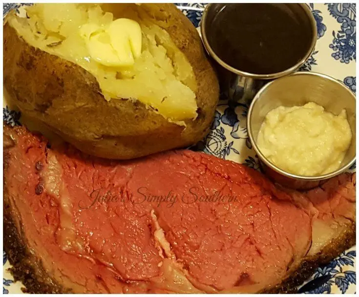Perfect Prime Rib served on a plate with a baked potato, au ju and horseradish cream