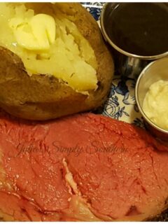 Perfect Prime Rib served on a plate with a baked potato, au ju and horseradish cream
