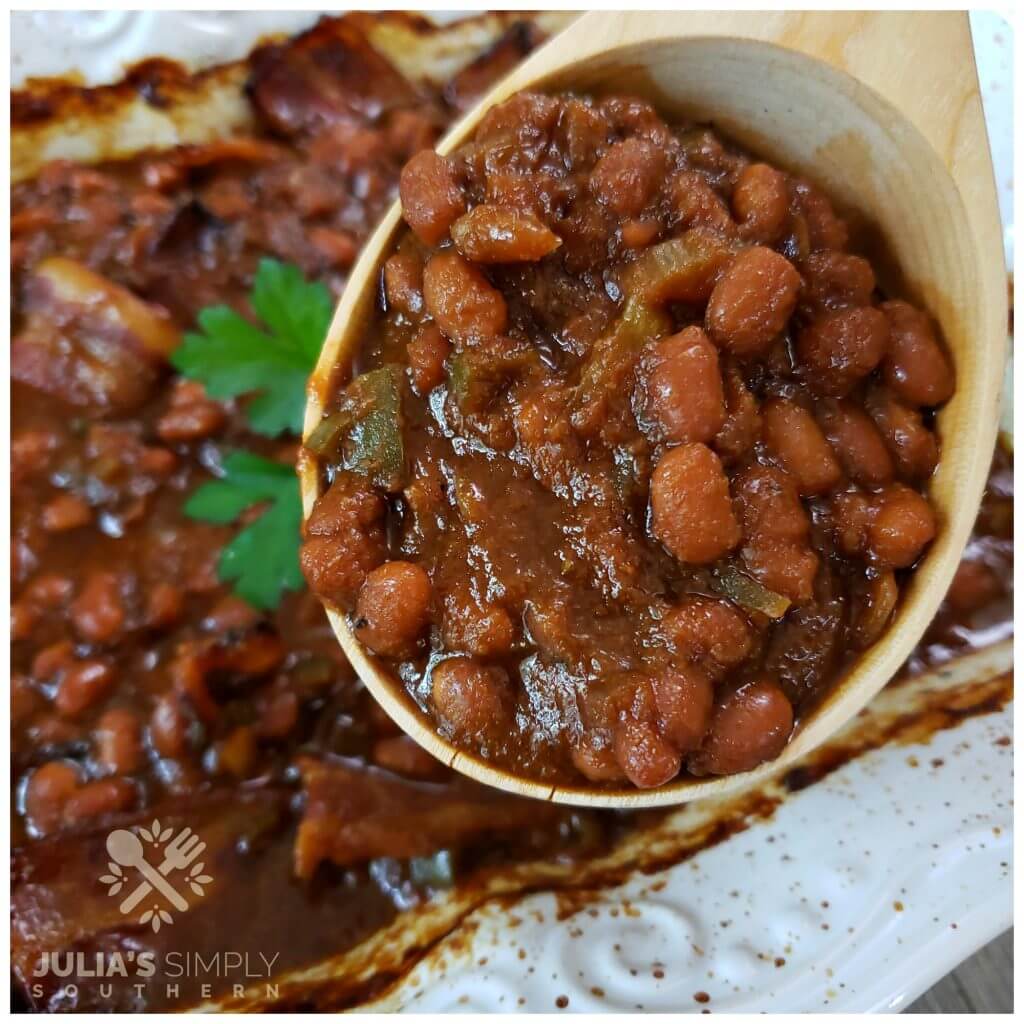 Homemade baked beans with bacon in a wooden serving spoon. Everyone loves this amazing side dish.