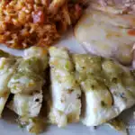 Amazing salsa verde chicken dinner topped with cheese and served with Spanish rice and refried beans