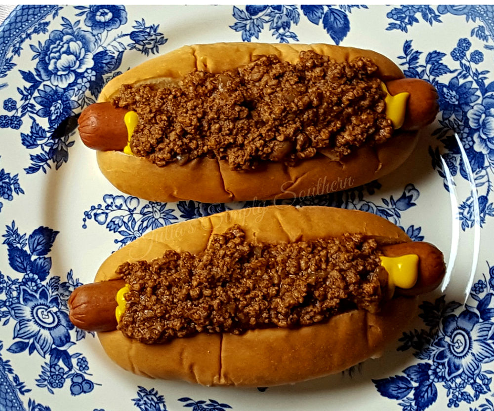 two hot dogs on a blue and white plate topped with chili sauce