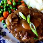 Blue and white plate with Salisbury Steak and mushroom gravy garnished with scallions