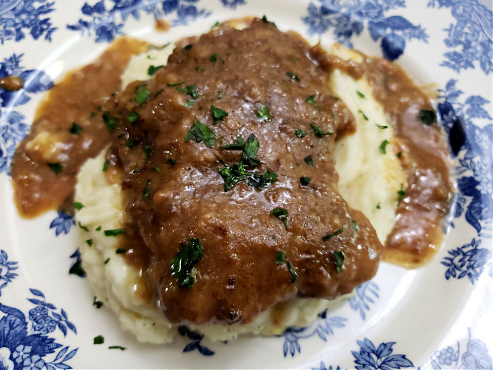 blue and white plate with creamy mashed potatoes topped with crock pot cube steak and homemade brown gravy