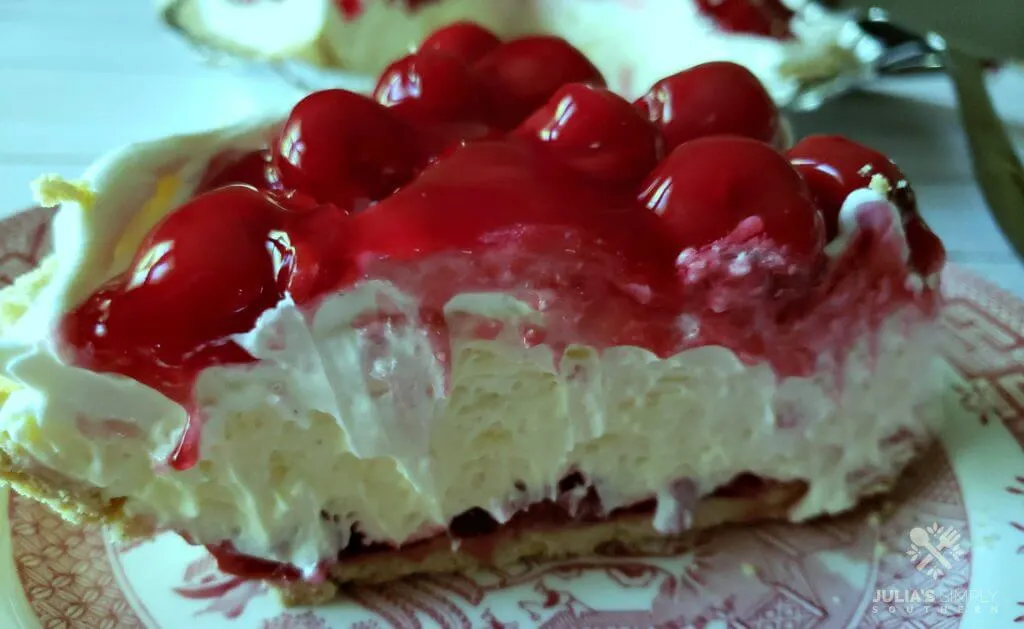 Side view of a layered cherry cheesecake pie, a no bake recipe, on a vintage red and white plate