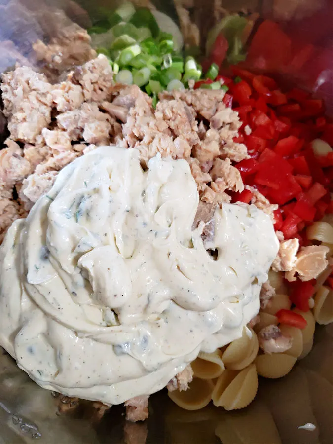 Mixing bowl with canned salmon, creamy mayo dressing and ingredients to mix for pasta salad
