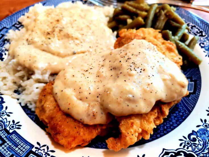 Herb Seasoned Southern Fried Boneless Chicken Breast on a plate with rice and gravy and green beans