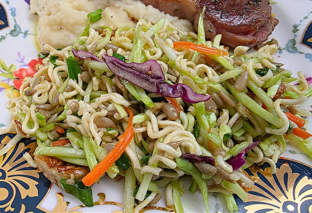 plate with a serving of broccoli slaw alongside lamb chops and mashed potatoes.