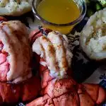 Broiled Lobster Tails on a serving platter with clarified butter, baked potatoes and asparagus