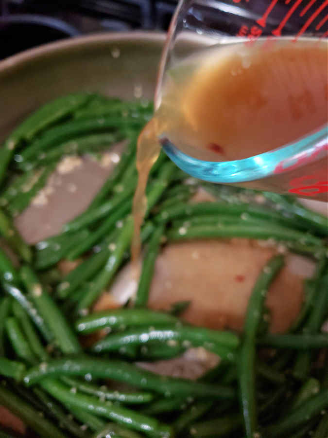 Pouring the sauté sauce into the skillet with green beans.