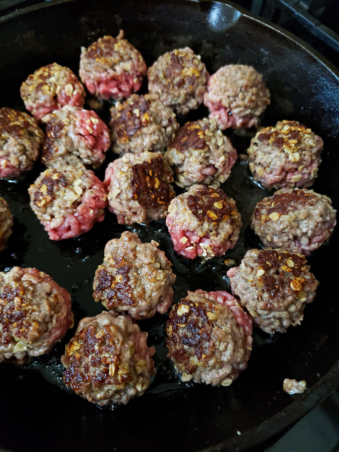 browning meatballs in a cast iron skillet on the stove top: easy old fashioned meatballs and gravy recipe