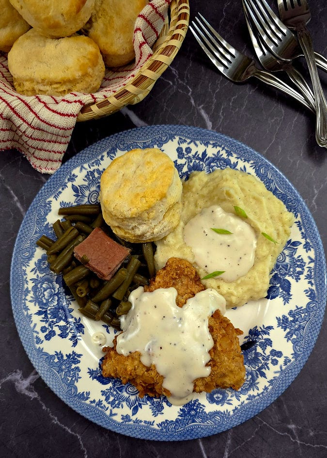 buttermilk mashed potatoes on a blue and white plate along with chicken fried chicken, green beans, and a biscuit