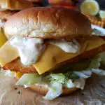Air Fryer Fish Sandwich Deluxe with crispy filet, homemade tartar sauce, cheese and toppings on toasted brioche bun