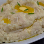 Creamy Southern Buttermilk Mashed Potatoes Recipe served in a white oval serving bowl with a drizzle of melted butter and chopped chives for garnish