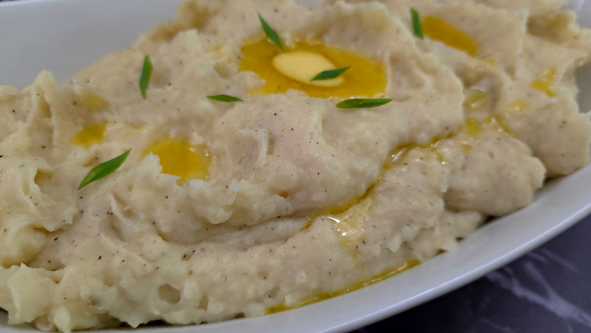 Creamy Southern Buttermilk Mashed Potatoes Recipe served in a white oval serving bowl with a drizzle of melted butter and chopped chives for garnish