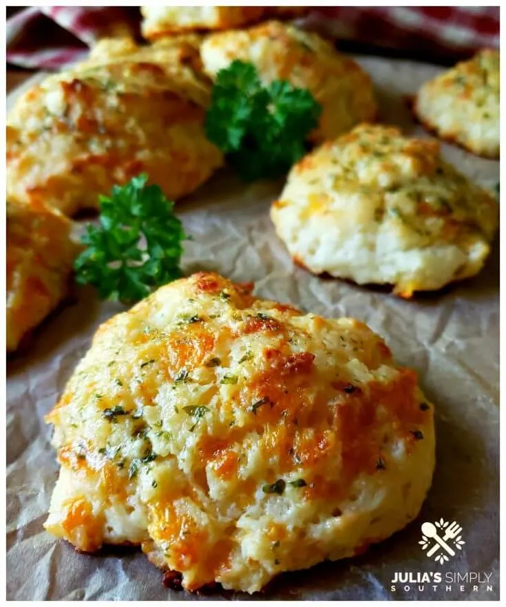 Garlic cheese drop biscuits brushed with an herb butter on a sheet of brown parchment with a few sprigs of parsley