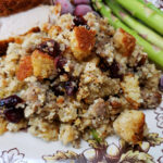 sage sausage cranberry pecan cornbread dressing served on a Thanksgiving plate with turkey and asparagus