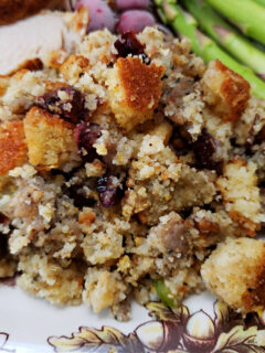 sage sausage cranberry pecan cornbread dressing served on a Thanksgiving plate with turkey and asparagus