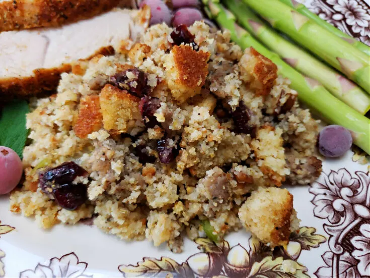 sage sausage cranberry pecan cornbread dressing served on a Thanksgiving plate with turkey and asparagus