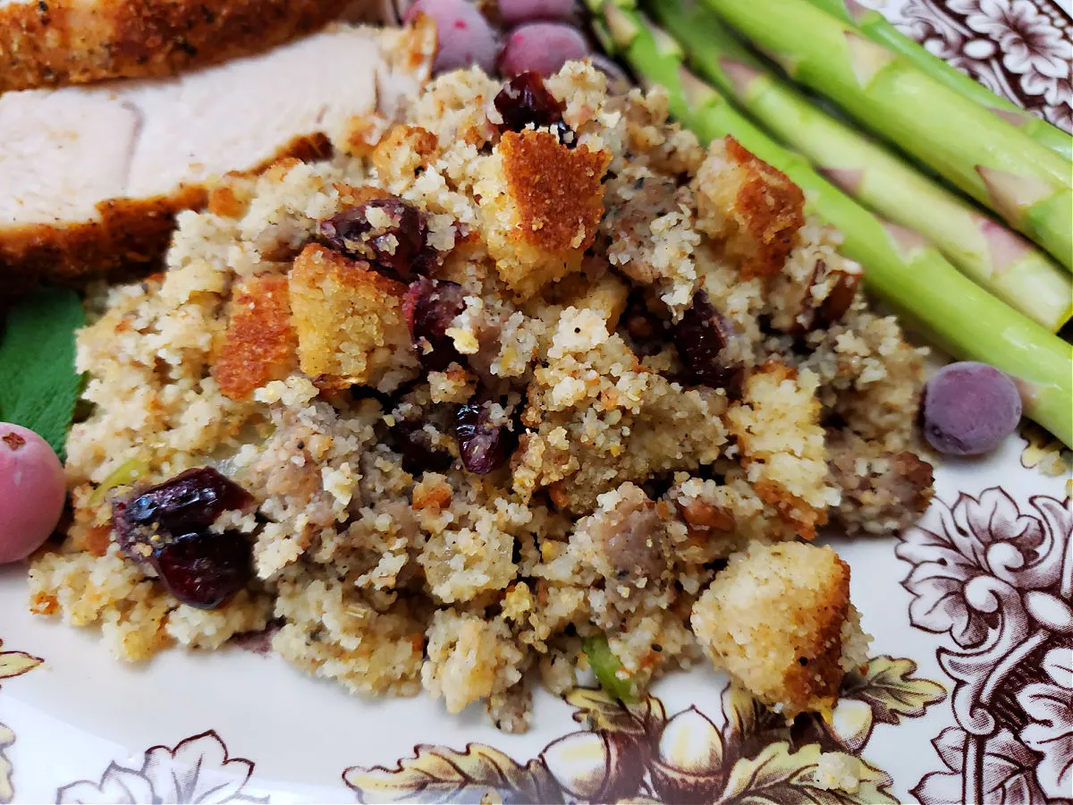 sage sausage cranberry pecan cornbread dressing served on a Thanksgiving plate with turkey and asparagus