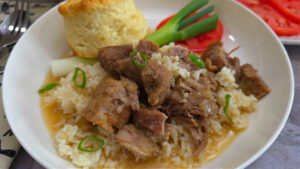 Country-Style Stewed Pork Meat and Rice Recipe with broth served in a white bowl with a buttermilk biscuit, green onion, and rip tomato slice