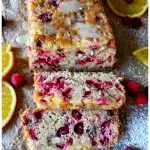 Cranberry Bread that has glaze and is dusted with confectioner's sugar and garnished with fresh cranberries and orange slices