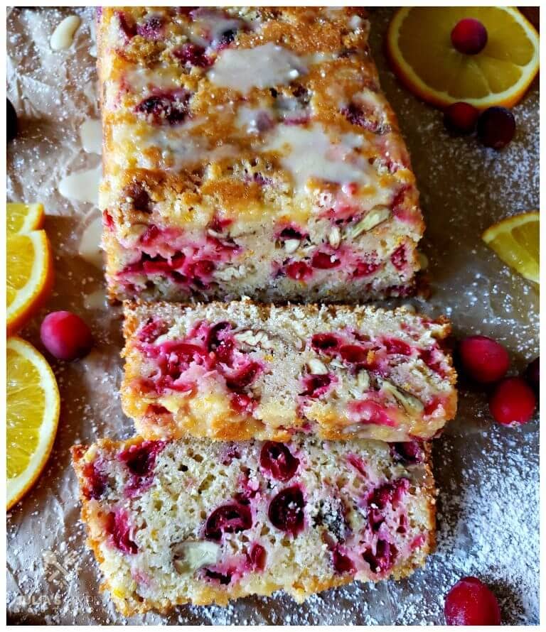 Cranberry Bread that has glaze and is dusted with confectioner's sugar and garnished with fresh cranberries and orange slices