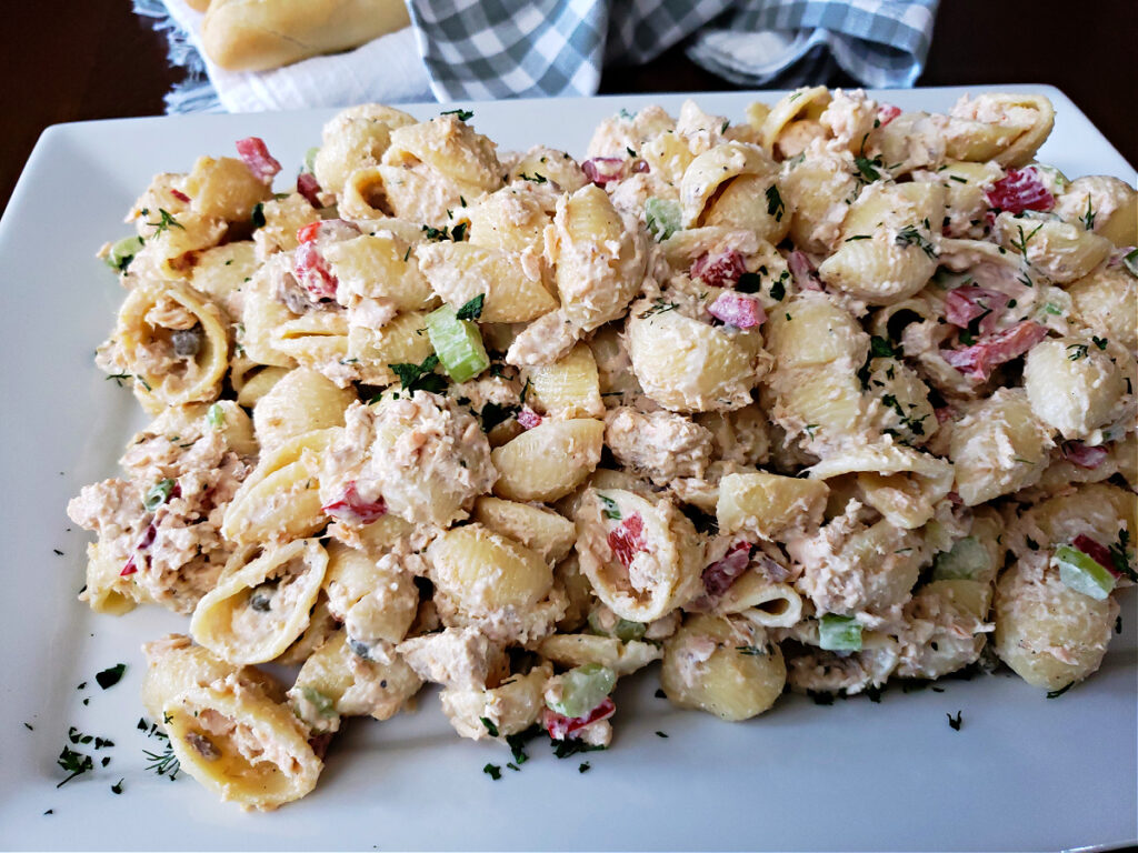 Canned salmon pasta salad with a creamy mayonnaise dressing on a white serving platter with bread in the background