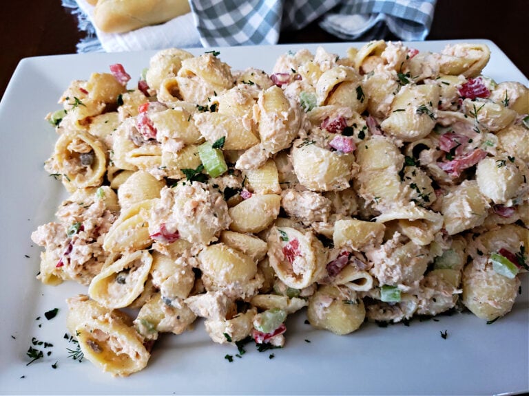 Canned salmon pasta salad with a creamy mayonnaise dressing on a white serving platter with bread in the background