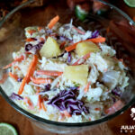 Pineapple coleslaw in a vintage glass bowl with pulled pork sandwiches in the background