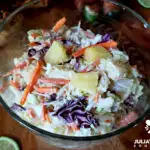 Pineapple coleslaw in a vintage glass bowl with pulled pork sandwiches in the background