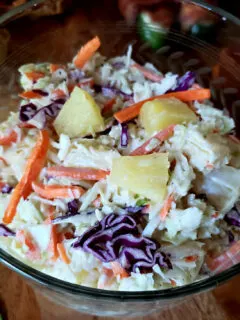 Pineapple coleslaw in a vintage glass bowl with pulled pork sandwiches in the background