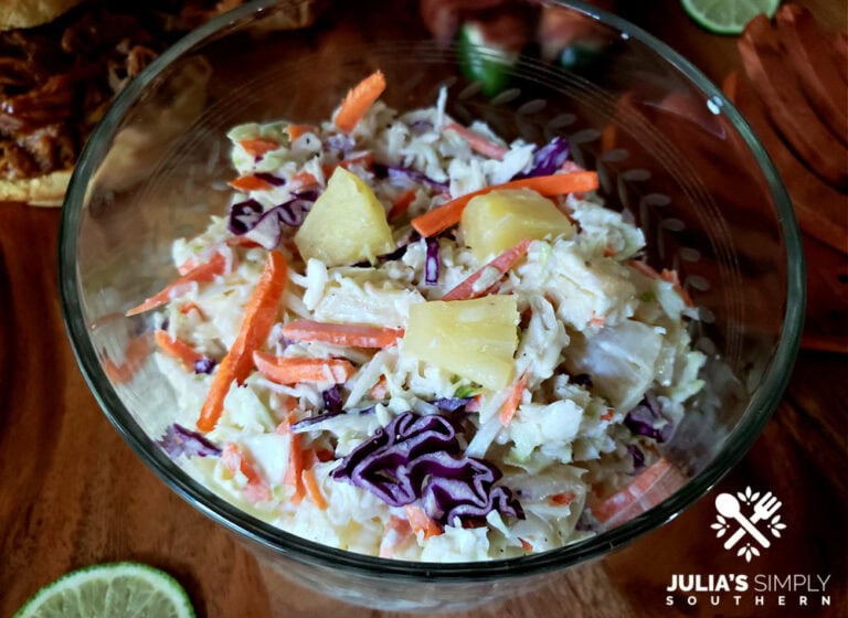 Pineapple coleslaw in a vintage glass bowl with pulled pork sandwiches in the background