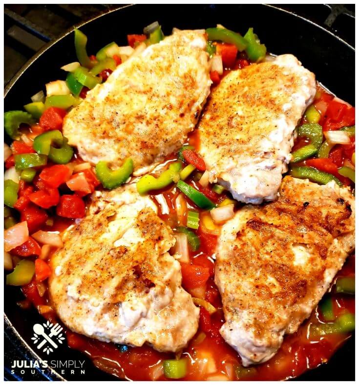 Creole Pork Chops Recipe in a cast iron skillet with the Cajun trinity and tomatoes