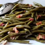 Southern green beans on a white serving platter topped with crispy bacon pieces