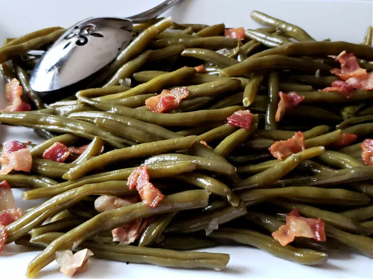 Southern green beans on a white serving platter topped with crispy bacon pieces