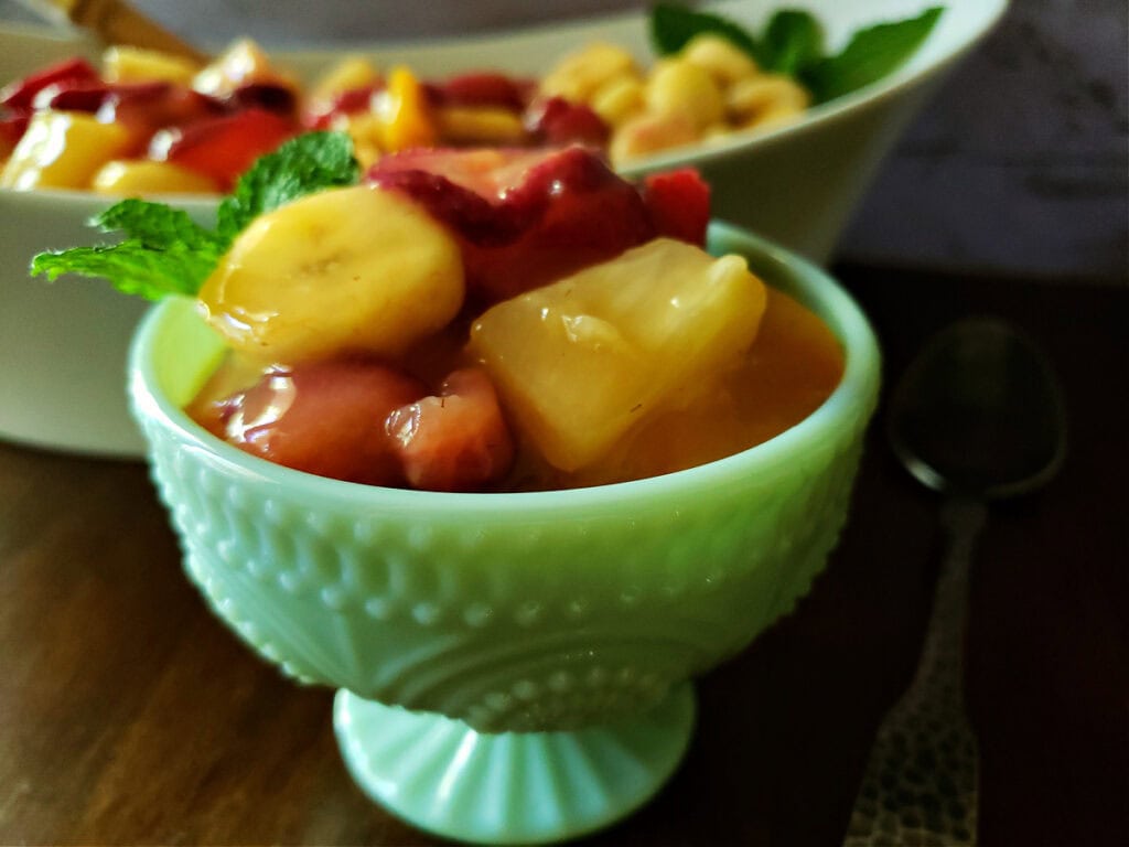 easy fruit salad recipe with vanilla pudding with strawberries, banana, peaches and pineapple in a jadeite serving dish.