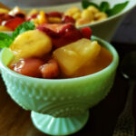 easy fruit salad recipe with vanilla pudding with strawberries, banana, peaches and pineapple in a jadeite serving dish.