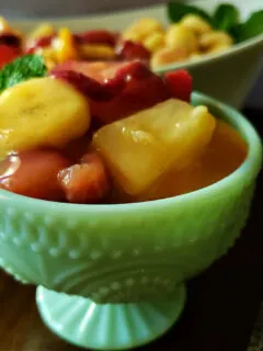 easy fruit salad recipe with vanilla pudding with strawberries, banana, peaches and pineapple in a jadeite serving dish.